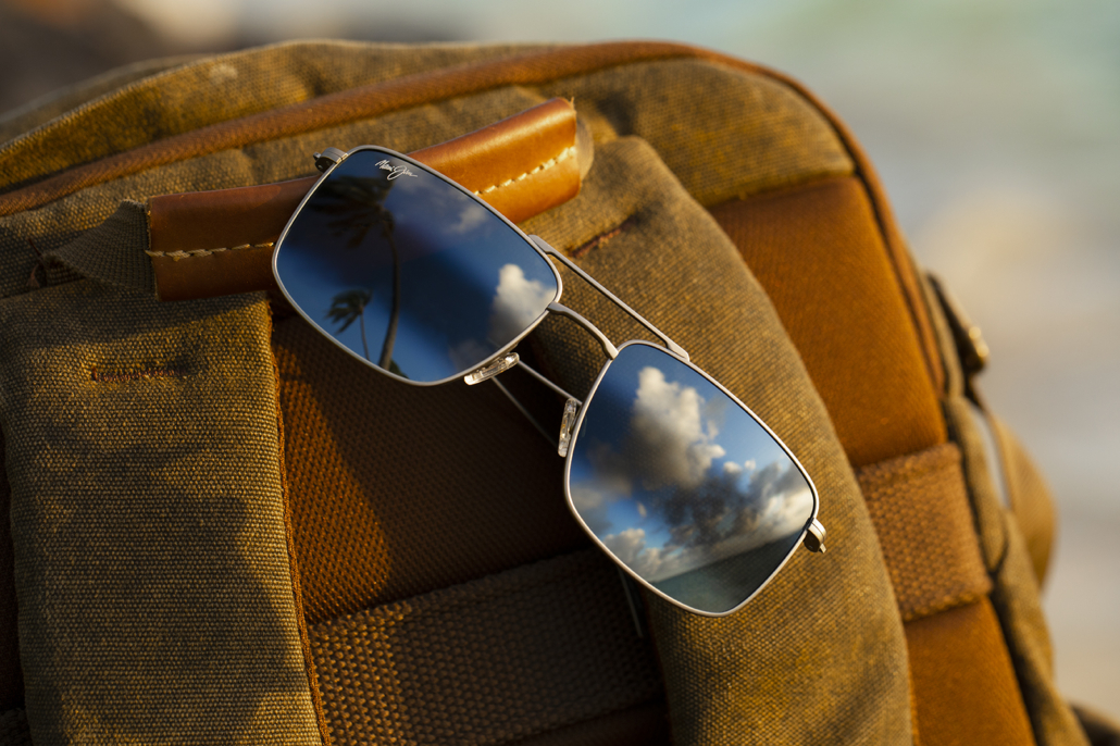 Aeko sunglasses with Matte Titanium frame and Neutral Grey lenses, resting on brown backpack