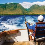 Man on a boat deep sea fishing, grass-covered mountains in distance