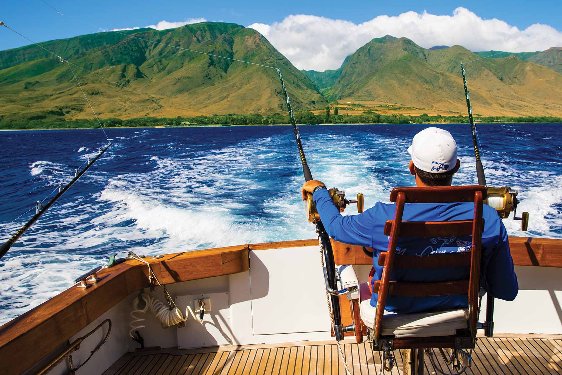 Man on a boat deep sea fishing, grass-covered mountains in distance
