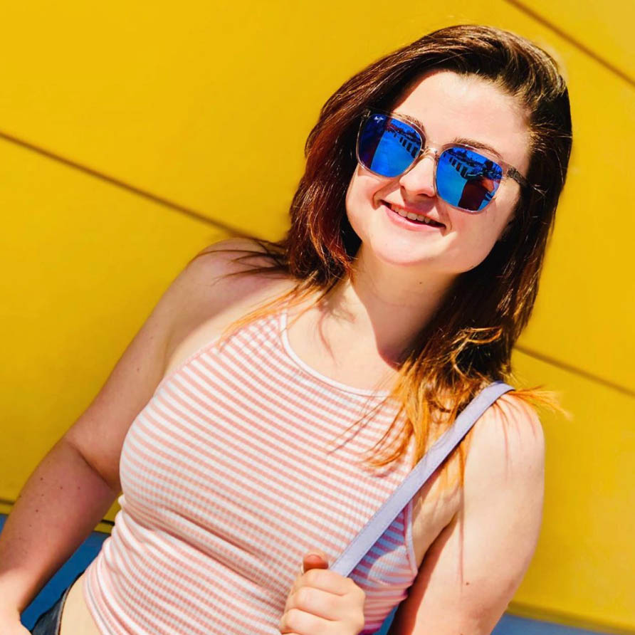 Woman in front of yellow wall wearing Crystal Westside Sunglasses with Blue Hawaii lenses