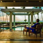 Man seated near pool with ocean background