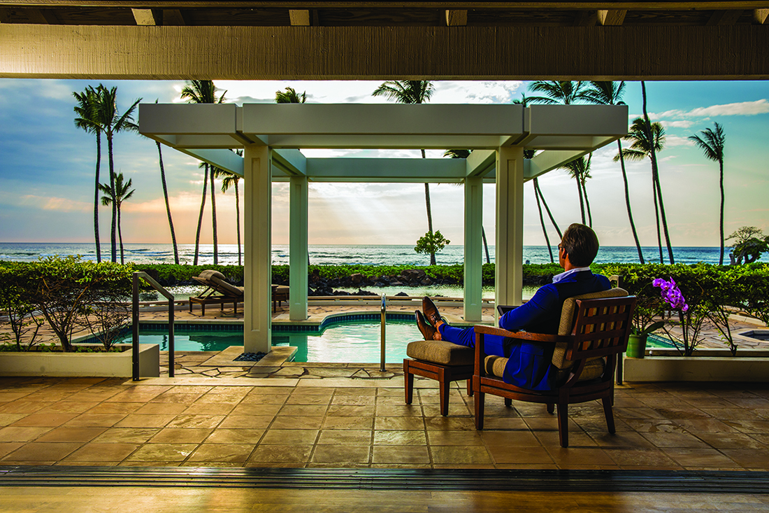 Man seated near pool with ocean background