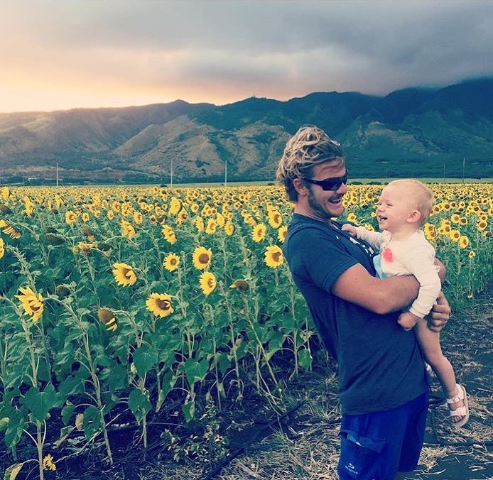 Man holding baby near sunflower field