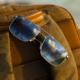 Aeko sunglasses with Matte Titanium frame and Neutral Grey lenses, resting on brown backpack