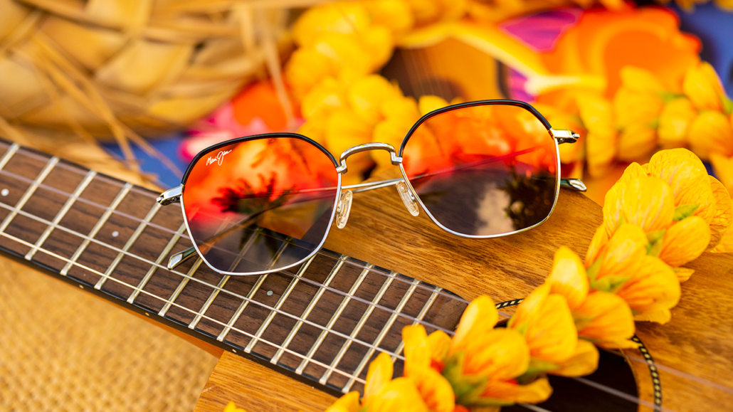 Polarized fashion sunglasses with HAWAII LAVA™ red lenses, resting on a guitar