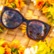 Brown fashion sunglasses resting on a woven basket, surrounded by flowers