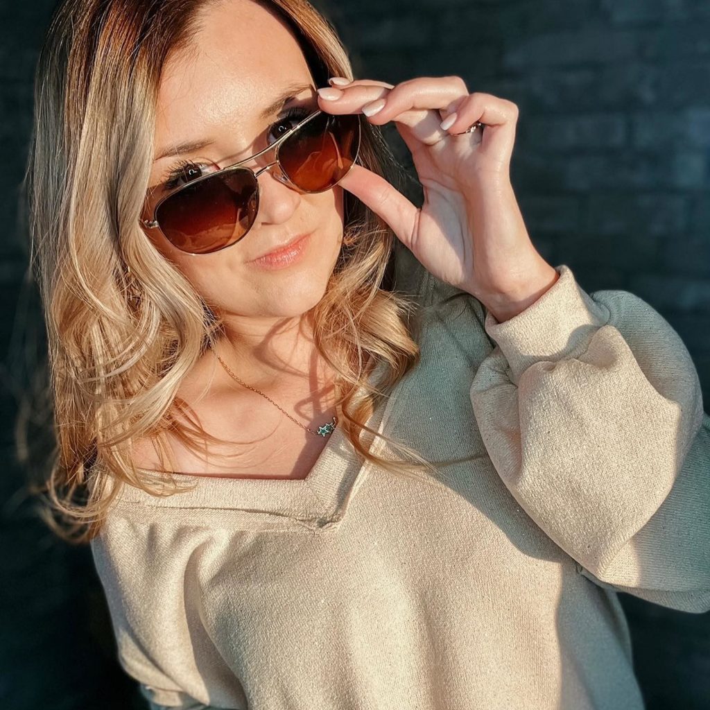 A woman taking a picture in sunlight next to a grey wall