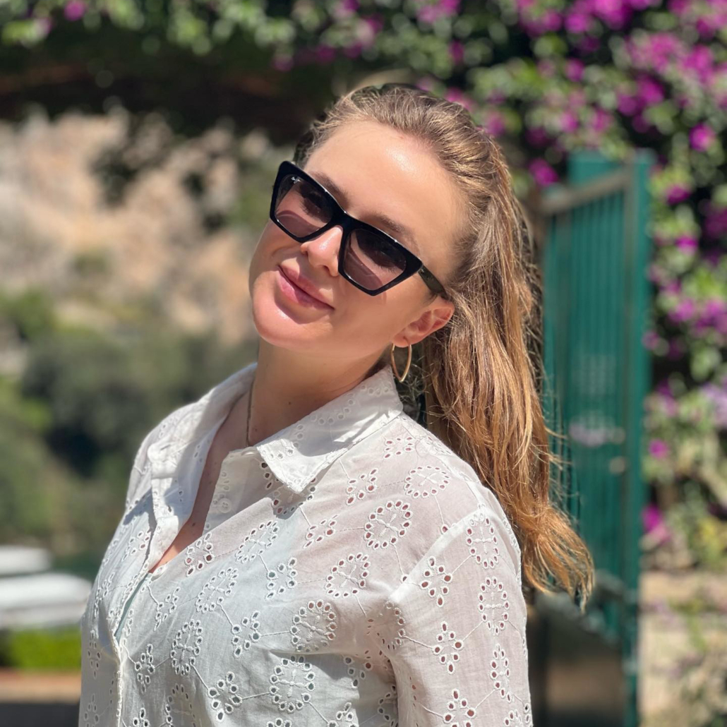 Blonde woman in white blouse poses in a pair of black fashion sunglasses