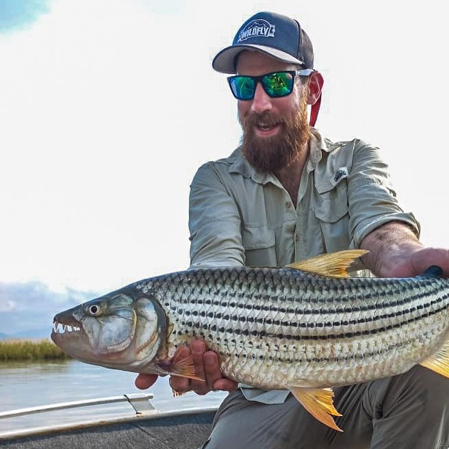 Man with oblong face wears black wrap sunglasses while holding a fish