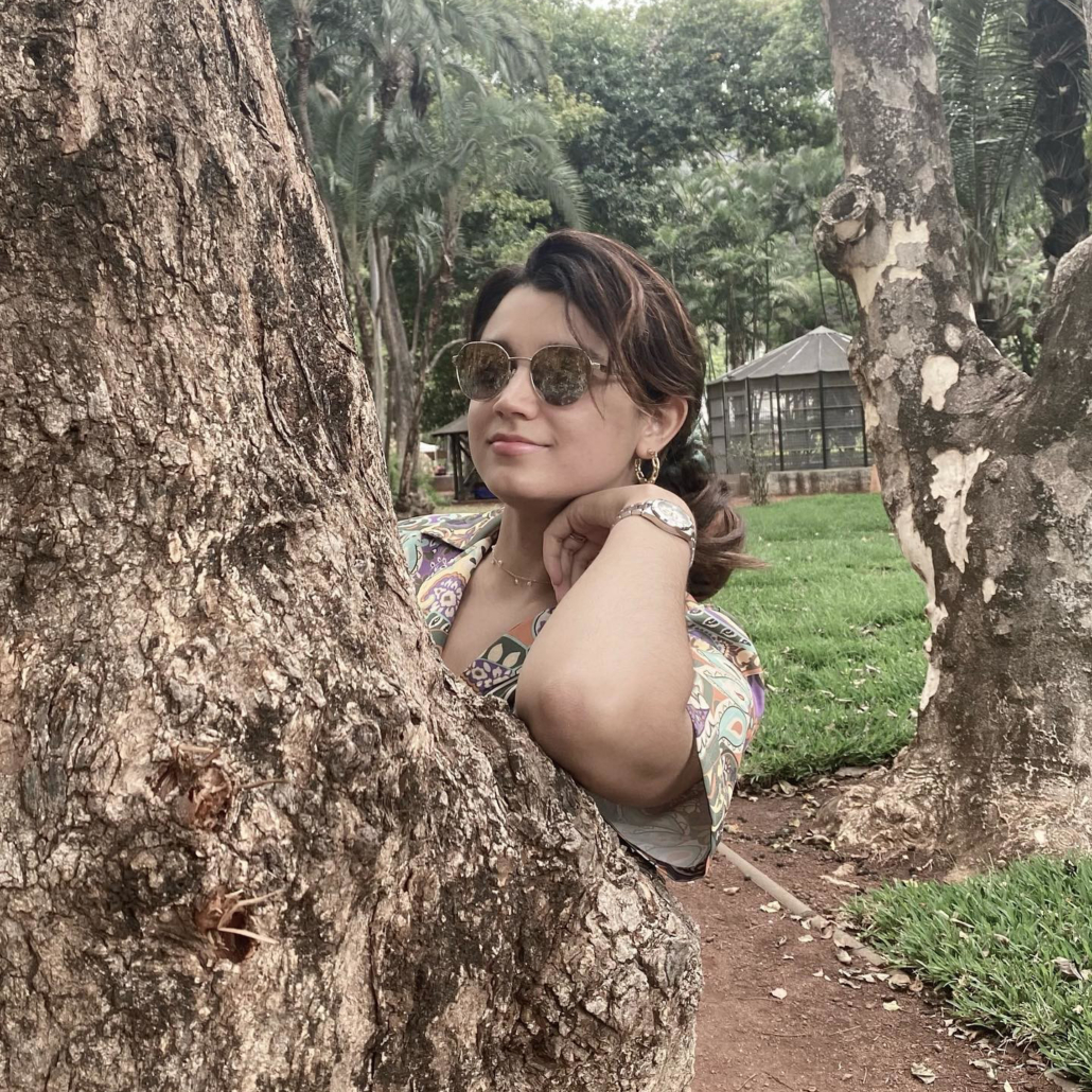 Woman in bronze aviators poses beside a tree