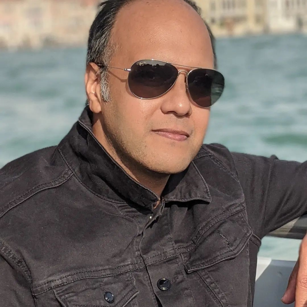 Man in silver aviators poses on a bridge