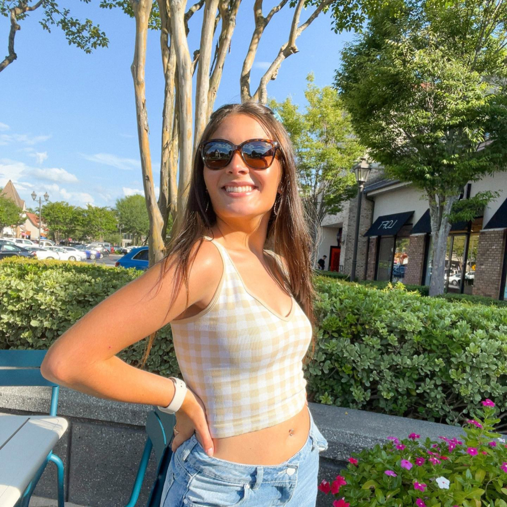 Woman in polarized fashion sunglasses poses in front of some colorful greenery