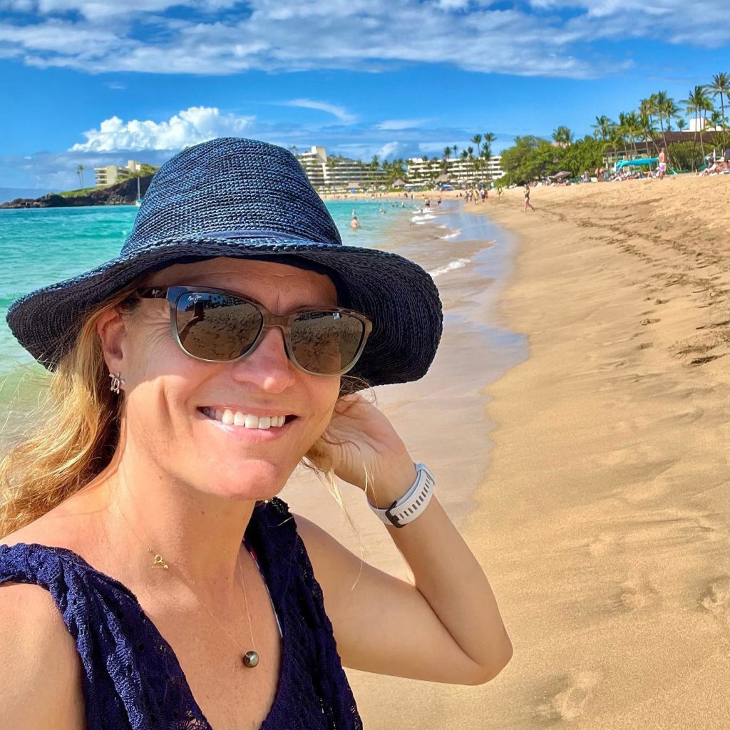 A woman posing next to a beach with a resort in the background