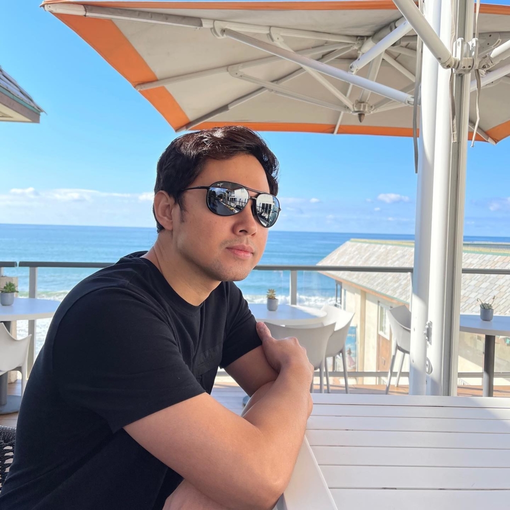 Man wearing black sunglasses sits at beachside table