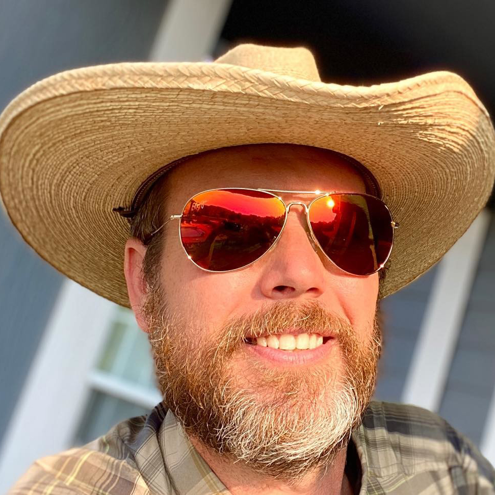 Man in a straw hat and aviator sunglasses with red mirror lenses poses for a selfie