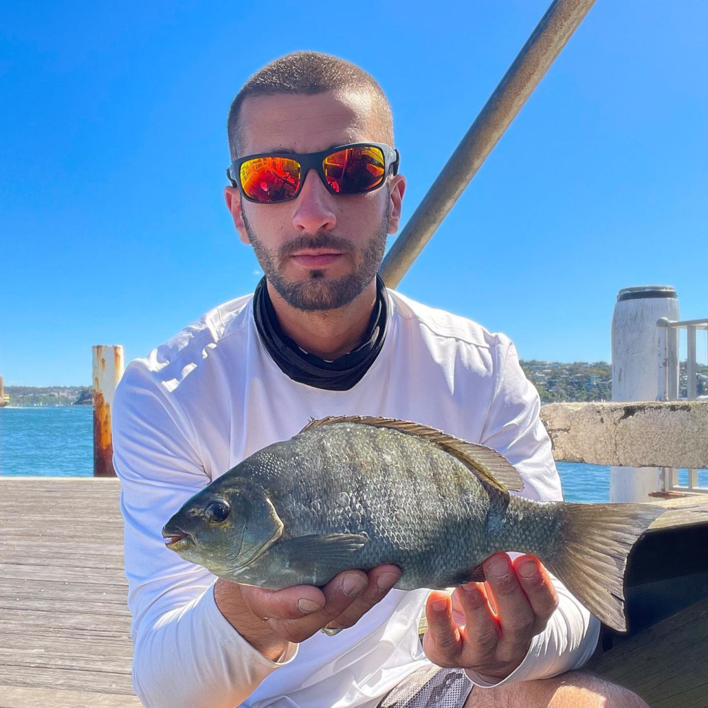 Man in red sunglasses and white shirt poses with a fish
