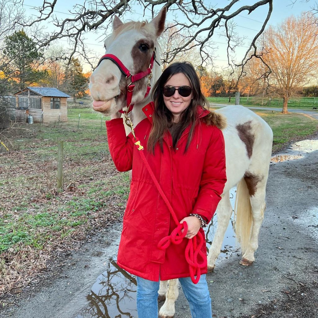 A woman in a red coat next to a pony