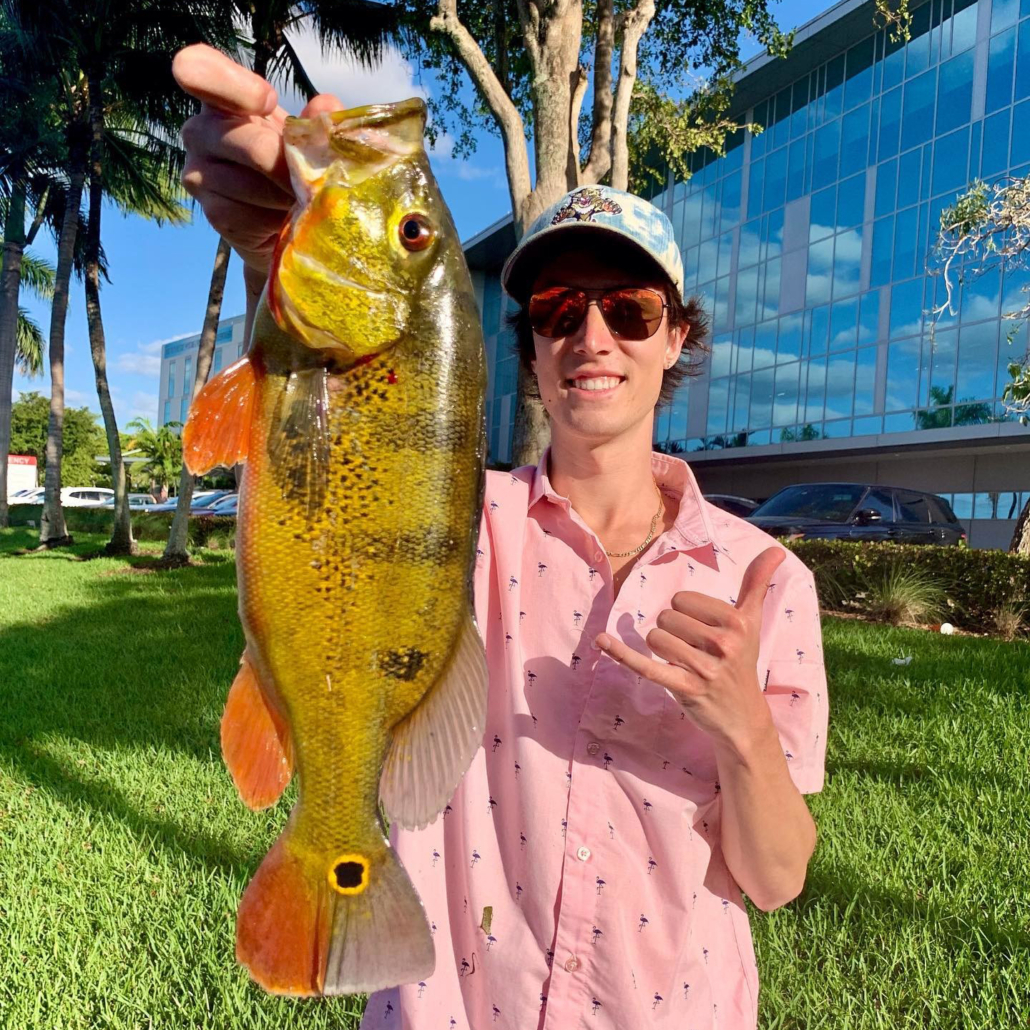 man holding fish next to a grassy parking lot